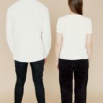 A diverse couple stands back to camera in casual white shirts, perfect for fashion concepts.