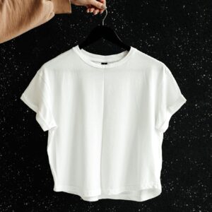 White t-shirt on hanger against a speckled black wall, showcasing minimalist fashion.